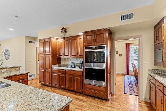 kitchen with light hardwood / wood-style floors, double oven, and light stone countertops