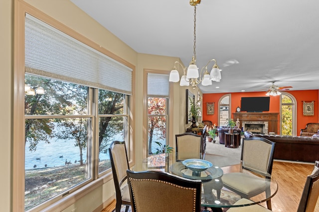 dining area featuring a water view, a wealth of natural light, ceiling fan with notable chandelier, and hardwood / wood-style floors