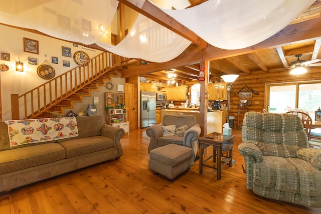 living room with light hardwood / wood-style flooring, ceiling fan, beamed ceiling, and rustic walls