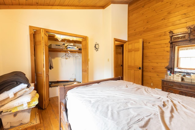 bedroom featuring wood ceiling, light hardwood / wood-style floors, lofted ceiling, a closet, and wood walls