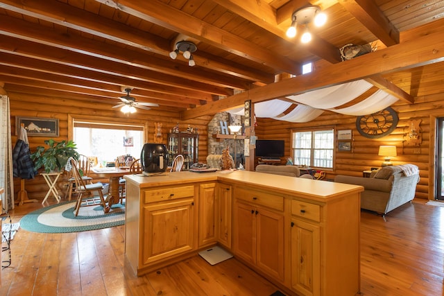 kitchen featuring ceiling fan, a fireplace, log walls, and beamed ceiling