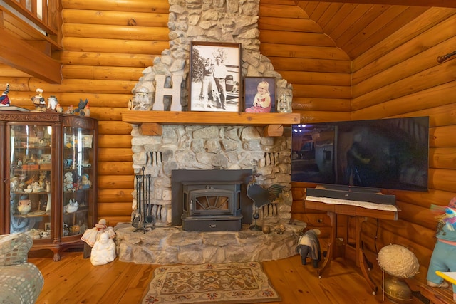 living room with hardwood / wood-style flooring, a wood stove, lofted ceiling, a stone fireplace, and rustic walls