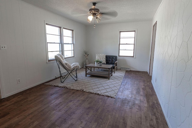 living area with ceiling fan, a textured ceiling, and dark wood-type flooring