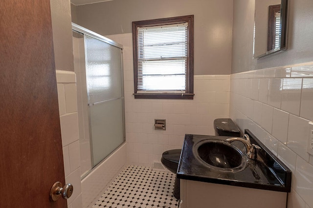 full bathroom featuring shower / bath combination with glass door, tile walls, vanity, and toilet