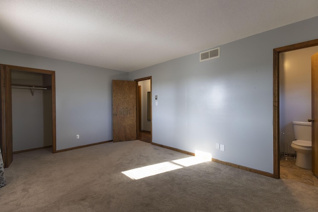 unfurnished bedroom featuring a textured ceiling, light colored carpet, ensuite bath, and a closet