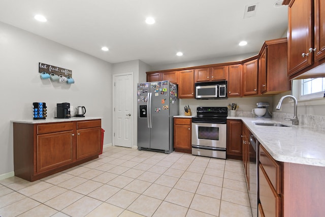 kitchen featuring light stone countertops, recessed lighting, a sink, brown cabinets, and appliances with stainless steel finishes