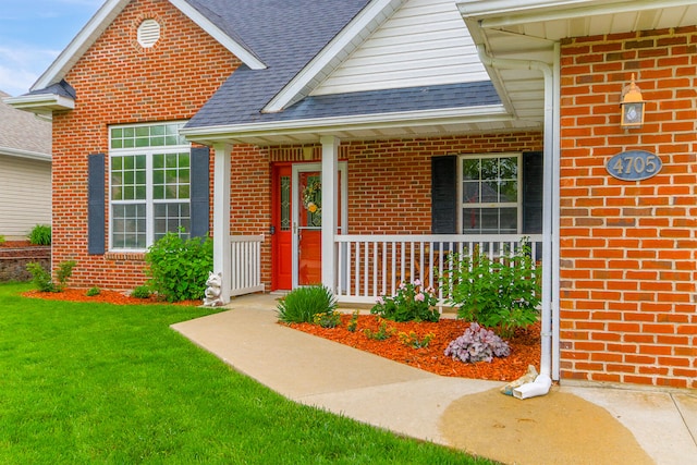 property entrance featuring covered porch, brick siding, roof with shingles, and a lawn