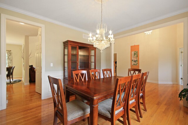 dining space featuring a notable chandelier, ornamental molding, and light hardwood / wood-style flooring