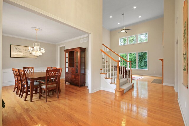 dining room featuring a high ceiling, ceiling fan with notable chandelier, light hardwood / wood-style flooring, and ornamental molding