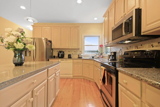 kitchen with tasteful backsplash, light wood-type flooring, appliances with stainless steel finishes, light brown cabinetry, and light stone countertops