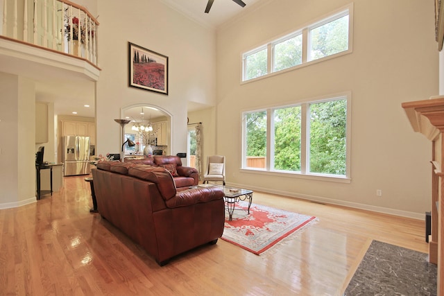 living room featuring a towering ceiling, ceiling fan with notable chandelier, crown molding, and light hardwood / wood-style floors