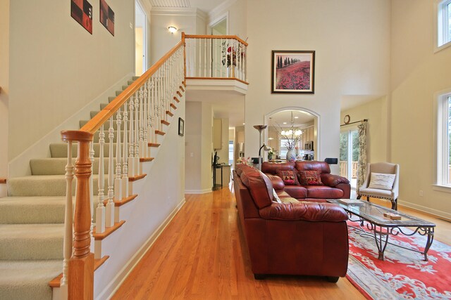 living room featuring a chandelier, wood-type flooring, ornamental molding, and a towering ceiling