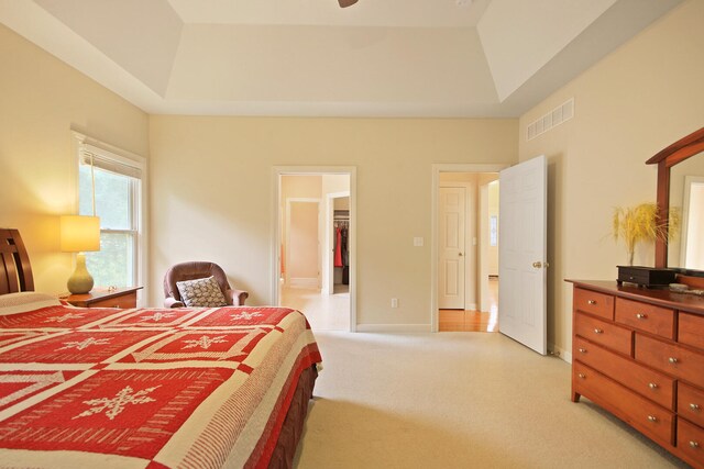 bedroom with light colored carpet, a closet, a spacious closet, and a tray ceiling