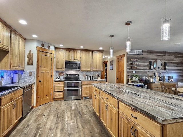 kitchen featuring hanging light fixtures, appliances with stainless steel finishes, wood walls, and hardwood / wood-style flooring