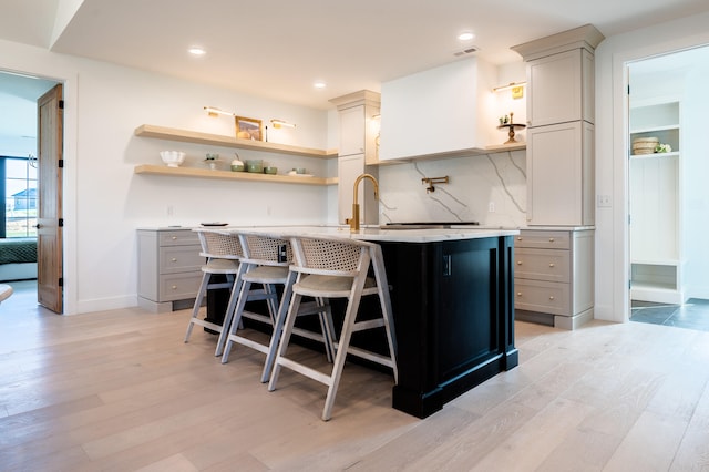 kitchen featuring an island with sink, gray cabinetry, a kitchen breakfast bar, light wood-type flooring, and decorative backsplash