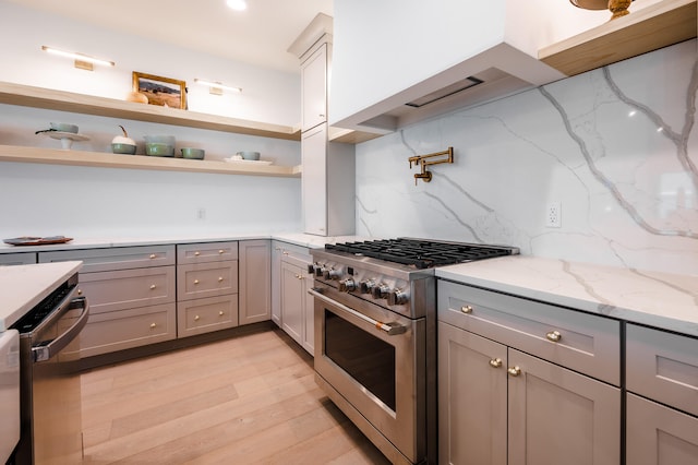 kitchen with gray cabinetry, light hardwood / wood-style flooring, stainless steel appliances, light stone countertops, and decorative backsplash