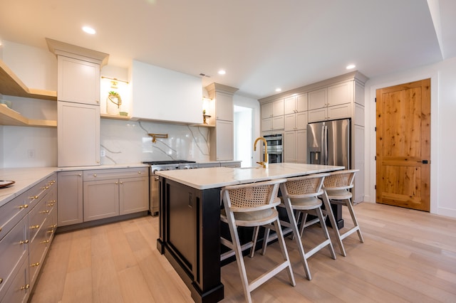 kitchen with an island with sink, gray cabinetry, light hardwood / wood-style flooring, a kitchen bar, and decorative backsplash