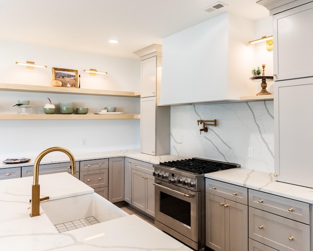 kitchen with sink, tasteful backsplash, gray cabinetry, stainless steel range, and light stone countertops