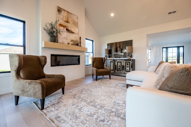 living room with high vaulted ceiling, hardwood / wood-style flooring, a large fireplace, and a wealth of natural light