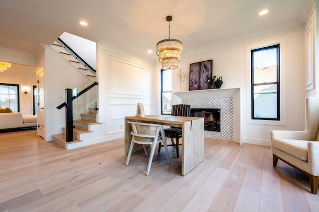 dining room with crown molding, a tiled fireplace, light hardwood / wood-style flooring, and a chandelier