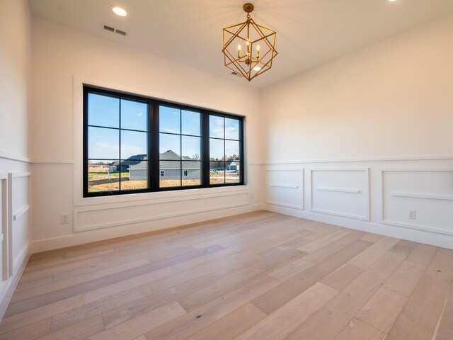 unfurnished room featuring a notable chandelier and light wood-type flooring