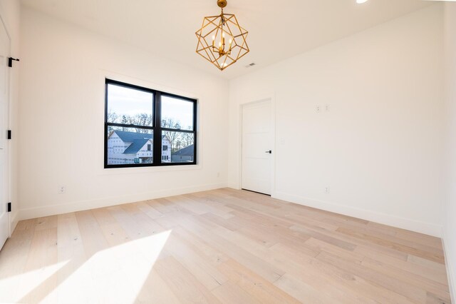 empty room with light hardwood / wood-style flooring and a notable chandelier