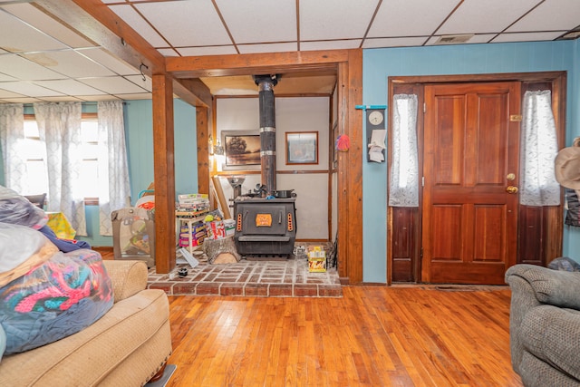 living room featuring a paneled ceiling, wood walls, a wood stove, and light hardwood / wood-style flooring