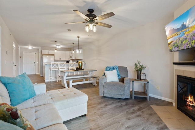 living room with wood-type flooring, a tiled fireplace, and ceiling fan