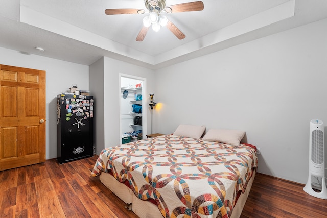 bedroom with a closet, black refrigerator, ceiling fan, a walk in closet, and dark hardwood / wood-style floors