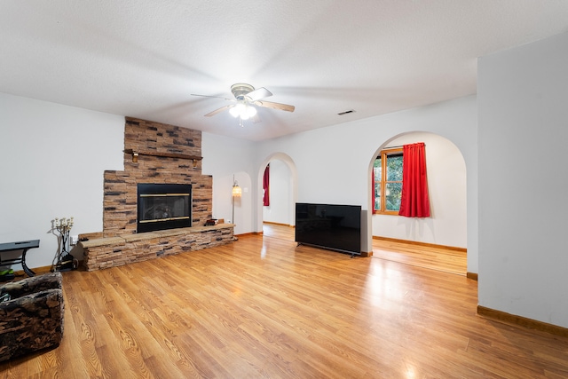 living room featuring a textured ceiling, ceiling fan, hardwood / wood-style flooring, and a stone fireplace