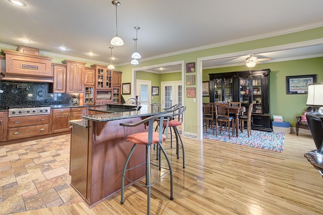 4200 S Rangeline Rd, Columbia, MO 65201 - kitchen featuring brown cabinets, stainless steel gas cooktop, a breakfast bar, custom range hood, and glass insert cabinets