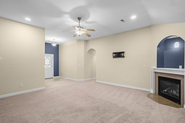 unfurnished living room with ceiling fan, light colored carpet, a premium fireplace, visible vents, and baseboards