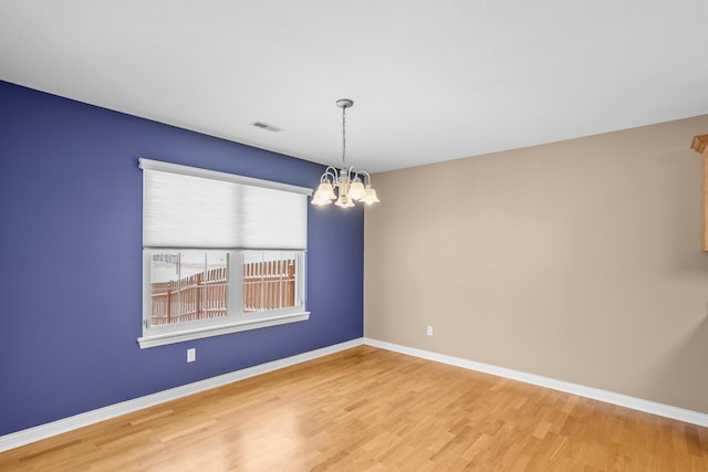 spare room with baseboards, wood finished floors, visible vents, and a notable chandelier