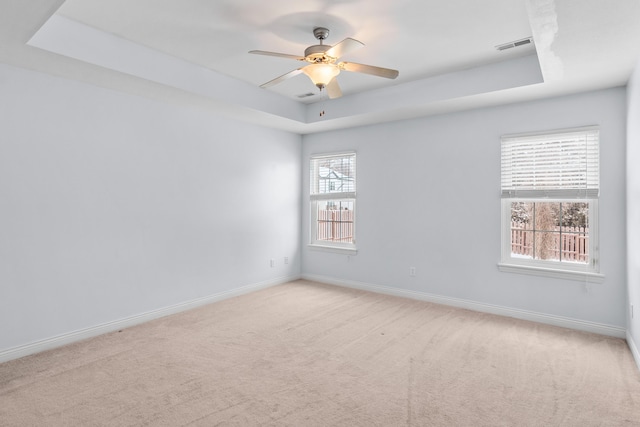 empty room with baseboards, a raised ceiling, a ceiling fan, and light colored carpet