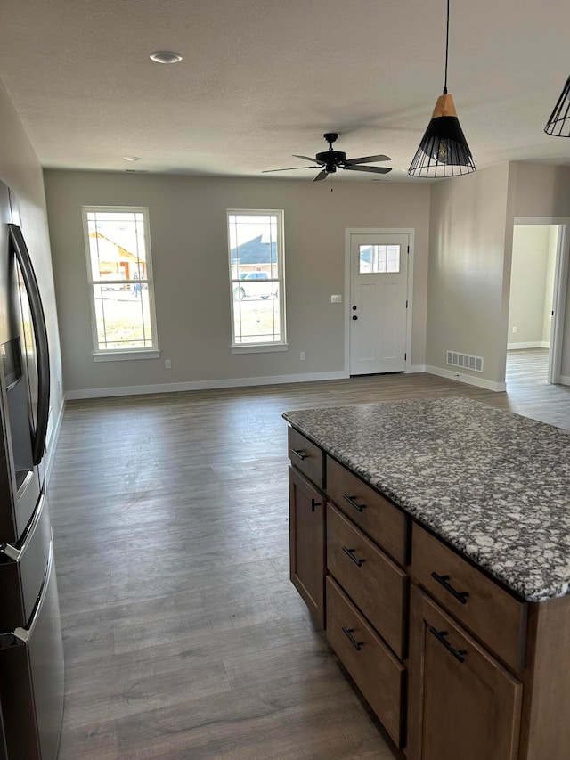 kitchen featuring ceiling fan, hanging light fixtures, stainless steel fridge with ice dispenser, dark stone countertops, and hardwood / wood-style floors