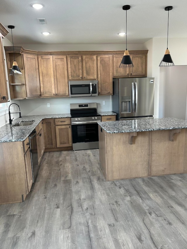 kitchen featuring appliances with stainless steel finishes, light stone counters, a breakfast bar, sink, and decorative light fixtures