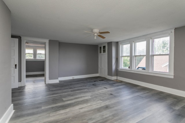 empty room featuring plenty of natural light, ceiling fan, dark hardwood / wood-style floors, and a textured ceiling