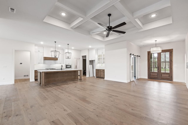 unfurnished living room with ceiling fan, beamed ceiling, coffered ceiling, a barn door, and light hardwood / wood-style floors