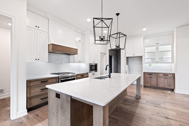 kitchen with sink, a kitchen island with sink, white cabinetry, stainless steel appliances, and light hardwood / wood-style floors