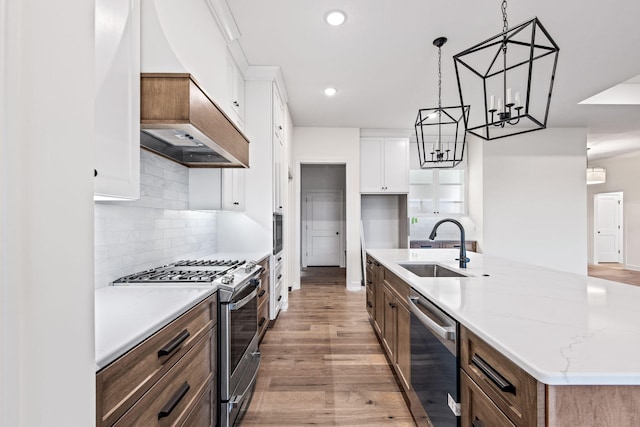 kitchen with pendant lighting, light hardwood / wood-style floors, white cabinetry, stainless steel appliances, and a center island with sink