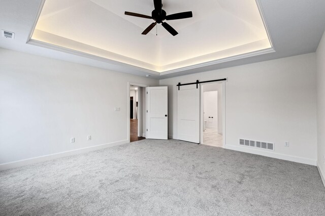 unfurnished bedroom featuring a barn door, a raised ceiling, light carpet, and ceiling fan