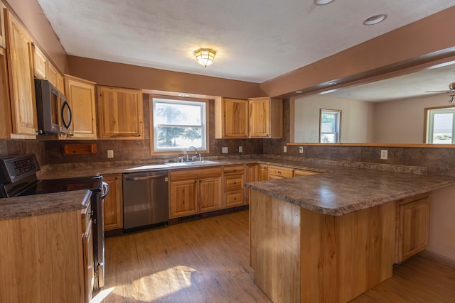 kitchen featuring appliances with stainless steel finishes, light wood-type flooring, kitchen peninsula, and decorative backsplash