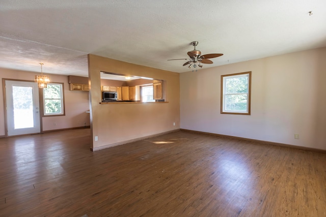 unfurnished room featuring ceiling fan with notable chandelier, a wealth of natural light, a textured ceiling, and dark hardwood / wood-style flooring