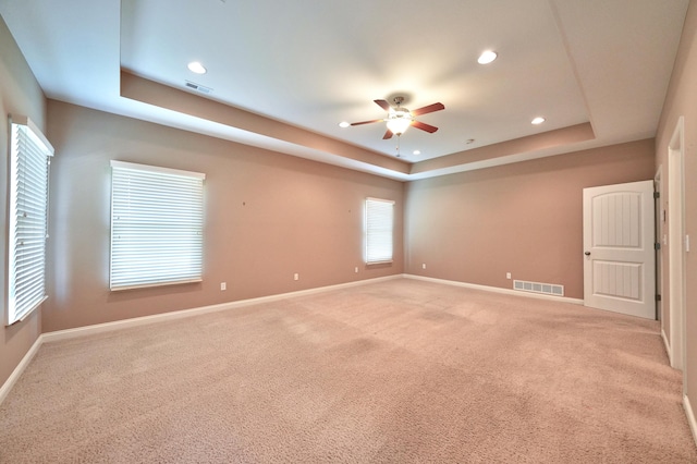 empty room featuring light colored carpet, ceiling fan, and a raised ceiling