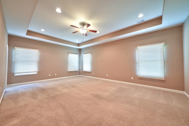 spare room featuring light colored carpet, ceiling fan, and a raised ceiling