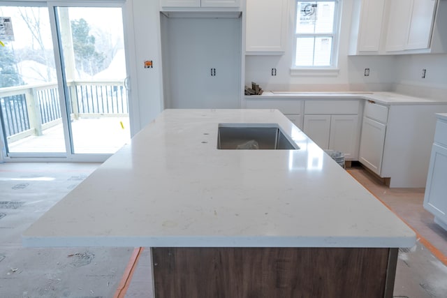 kitchen featuring light stone counters, black stovetop, a center island with sink, and white cabinets