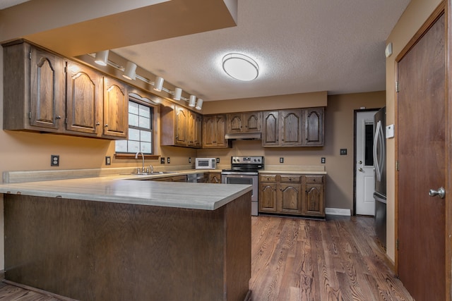 kitchen with stainless steel appliances, track lighting, dark hardwood / wood-style floors, sink, and kitchen peninsula