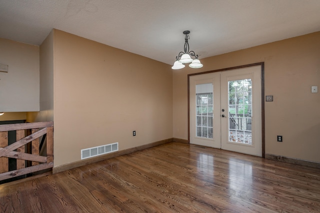 unfurnished dining area with wood-type flooring, a textured ceiling, a chandelier, and french doors