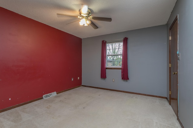 empty room featuring a textured ceiling, light colored carpet, and ceiling fan