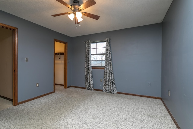 unfurnished bedroom featuring a textured ceiling, carpet flooring, a spacious closet, and ceiling fan